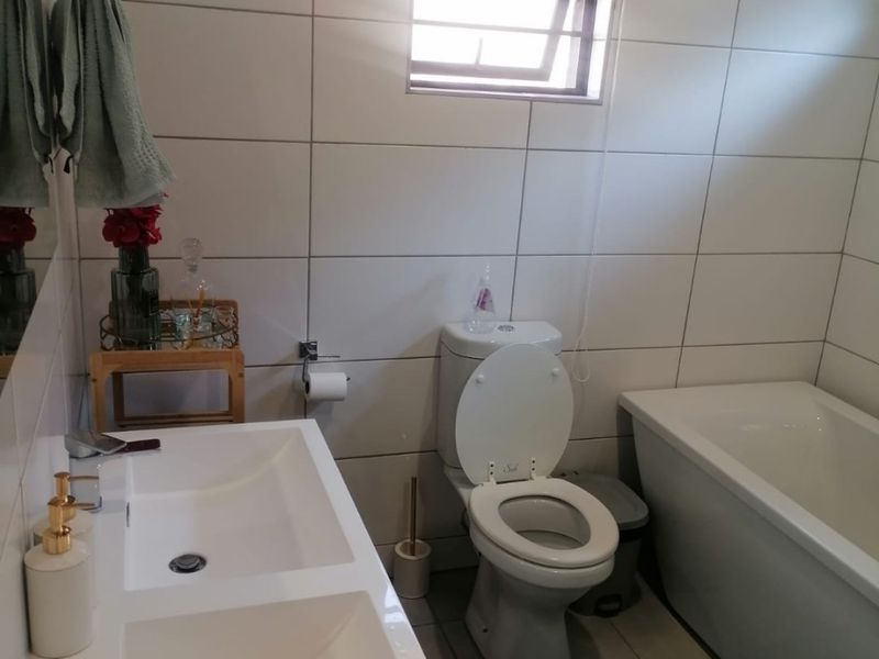 A modern bathroom featuring a double vanity, a built-in bathtub, and floor-to-ceiling wall tiles with a window for natural light.