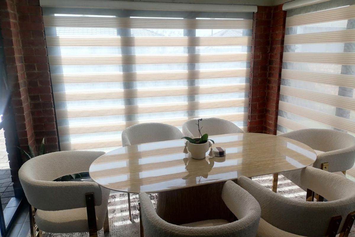 A bright dining area featuring exposed brick walls and large windows with modern roller blinds, creating a warm and inviting atmosphere.