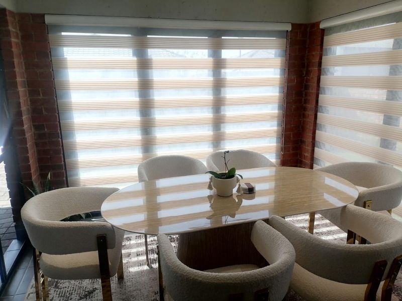 A bright dining area featuring exposed brick walls and large windows with modern roller blinds, creating a warm and inviting atmosphere.