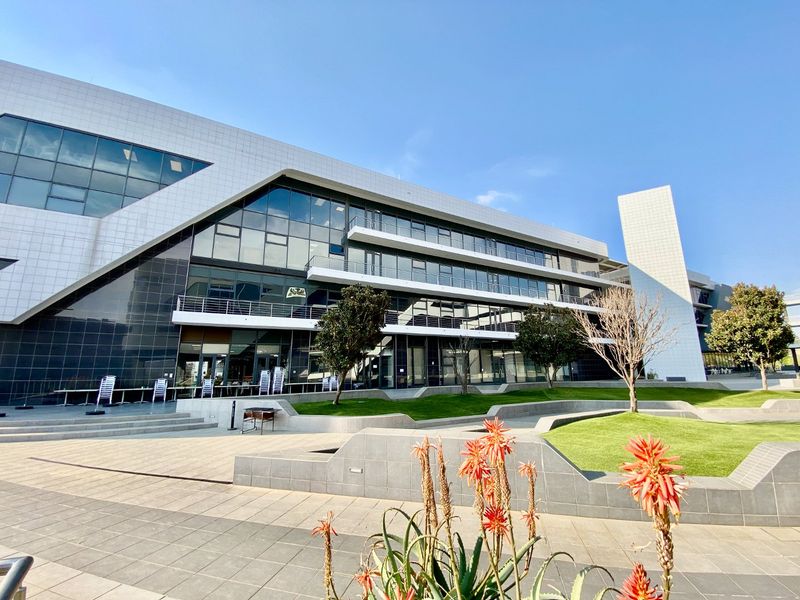 Modern commercial building exterior featuring a glass curtain wall, multi-level balconies, and a well-maintained landscaped garden with paved terrace areas.