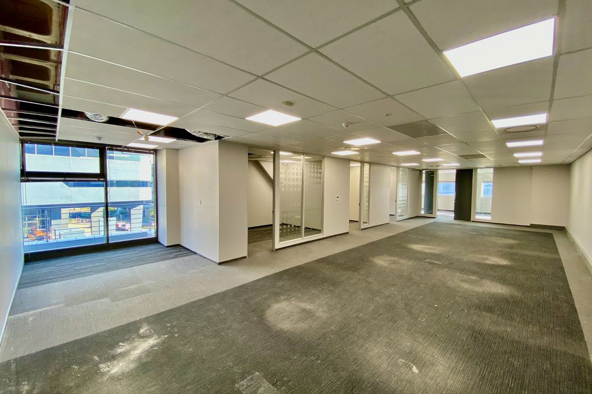 An open-plan commercial office space featuring glass partitions, suspended ceilings, and large windows, currently in need of refurbishment and carpet replacement.