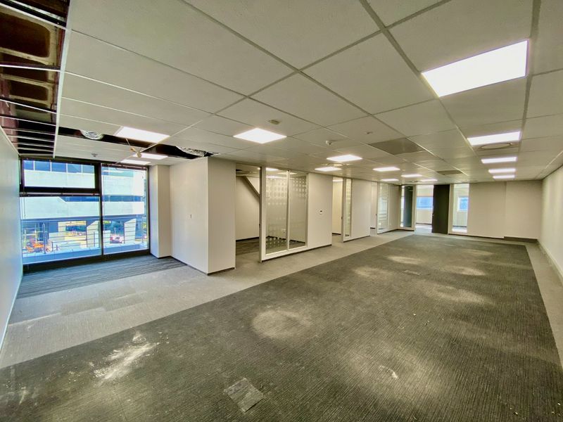 An open-plan commercial office space featuring glass partitions, suspended ceilings, and large windows, currently in need of refurbishment and carpet replacement.
