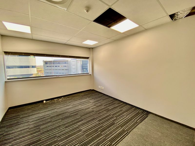 An empty commercial office space featuring carpeted flooring, recessed lighting, and a large window with blinds, requiring minor ceiling repairs.