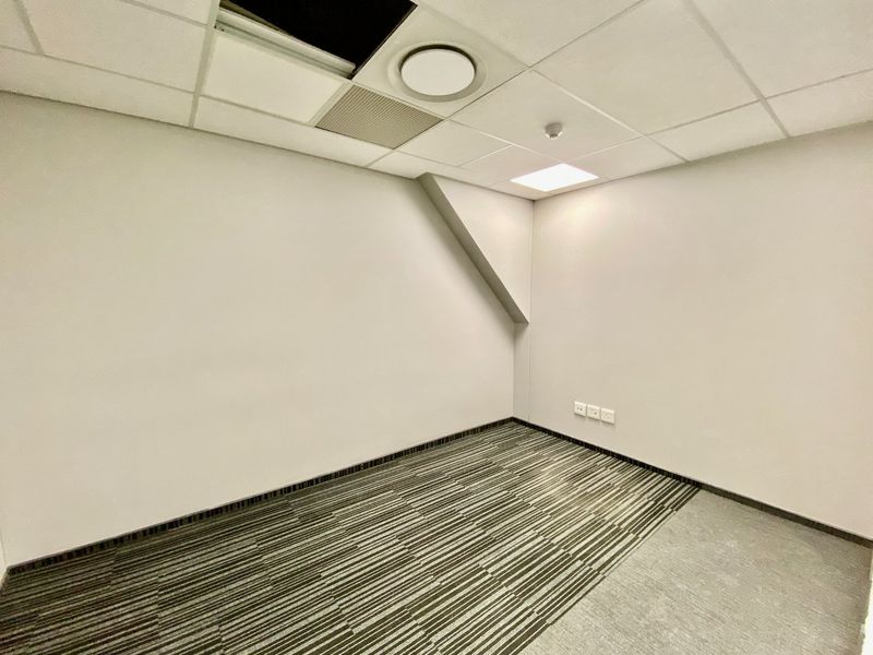 A vacant commercial office space featuring carpeted flooring, a suspended ceiling with recessed lighting, and integrated air conditioning infrastructure.