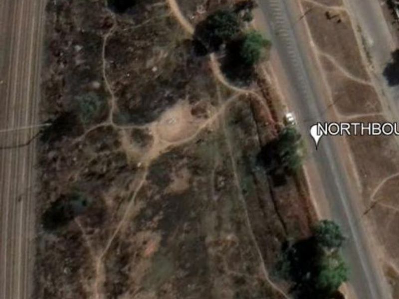 Aerial view of a vacant residential plot situated adjacent to a main road and railway line.