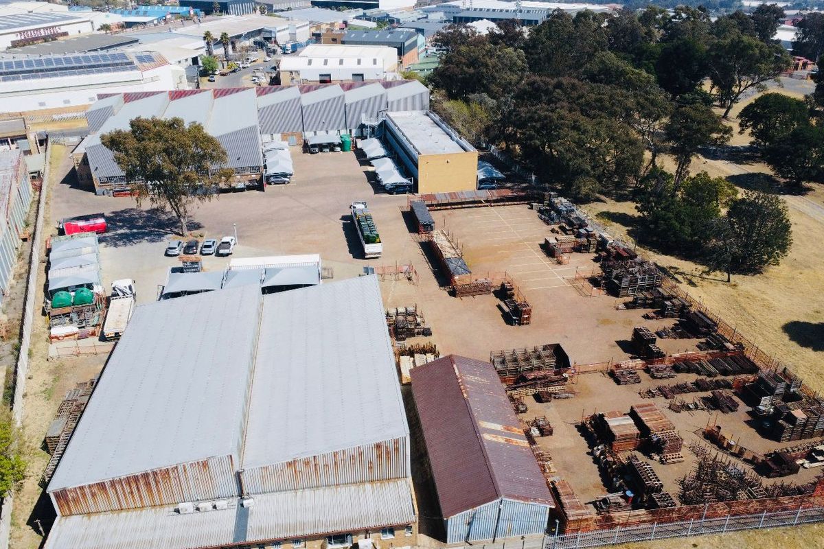 Aerial view of an industrial property featuring multiple warehouse buildings, extensive paved yard space, and perimeter fencing in a commercial industrial park setting.