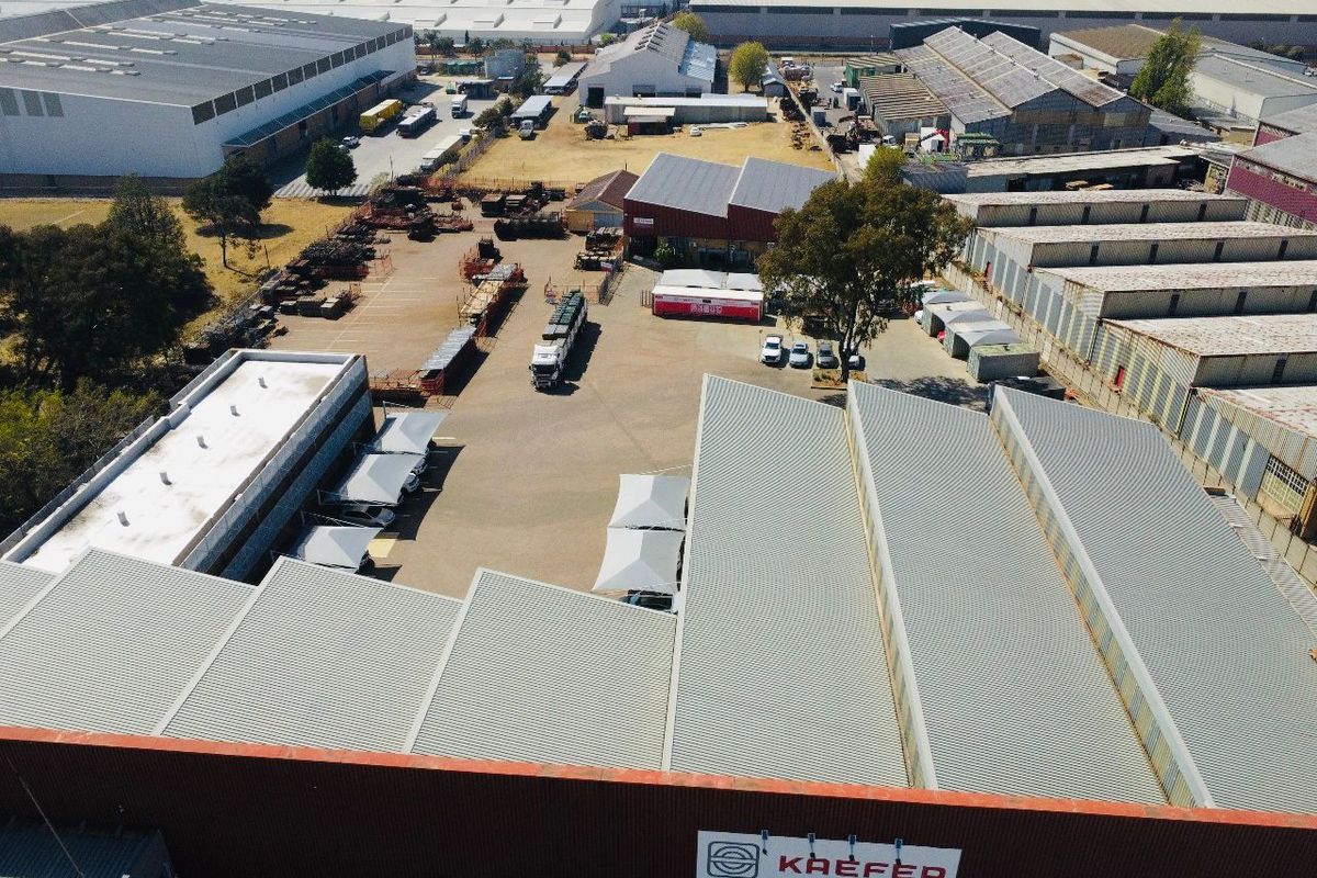Aerial view of an industrial property featuring multiple warehouse buildings, extensive paved yard space, and covered parking areas.