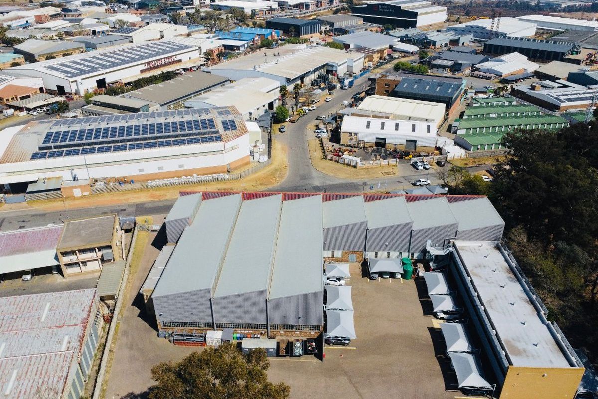 Aerial view of an industrial property featuring a large warehouse facility, paved parking area with shade cloth carports, and surrounding industrial infrastructure.