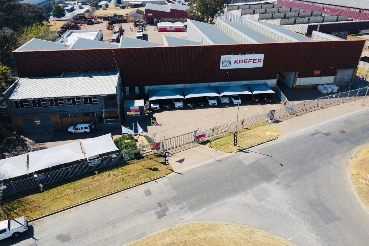 Aerial view of an industrial property featuring a large warehouse facility, secure perimeter fencing, paved driveway, and covered parking bays.