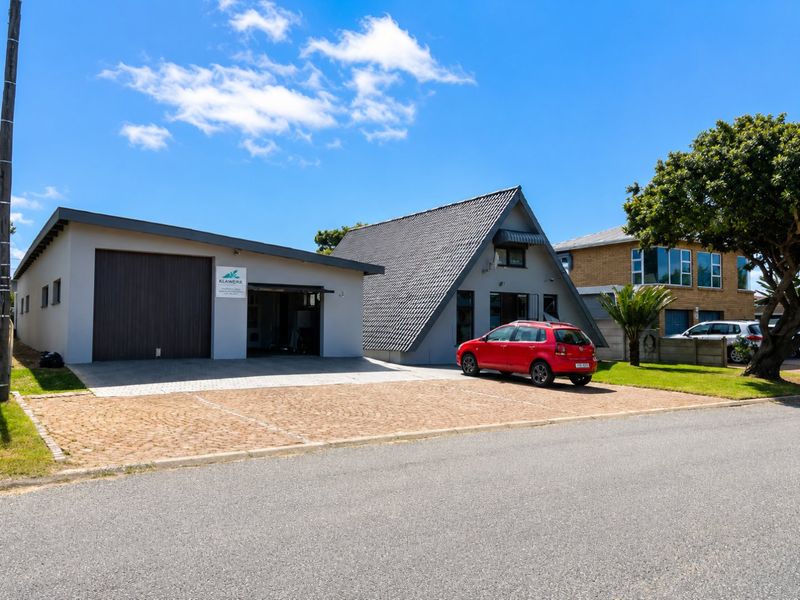 Front view of the property featuring a paved driveway, a garage, and a distinctive A-frame style roof structure.
