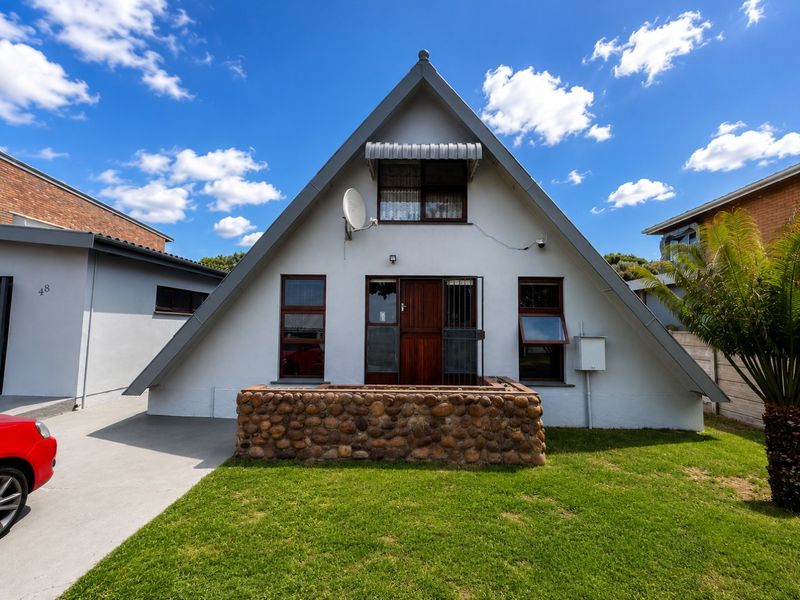 Front elevation of a distinctive A-frame house featuring a stone-clad planter box, timber entrance door, and a well-maintained front lawn.