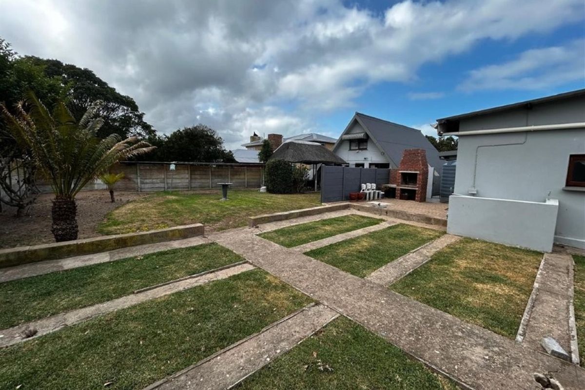Rear garden featuring a paved patio area with a built-in brick braai, lawn sections, and perimeter fencing.