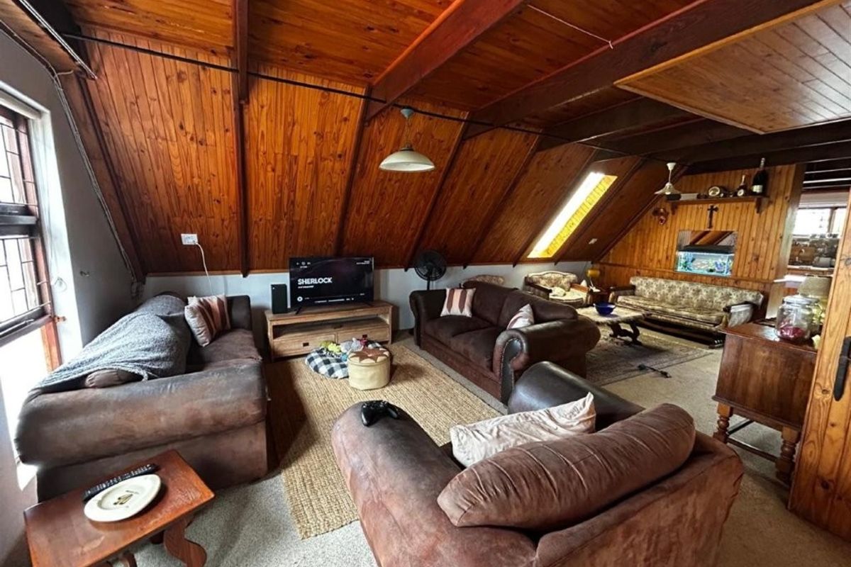Spacious living area featuring a vaulted timber ceiling with exposed beams, wood-paneled walls, and a skylight, creating a warm and rustic atmosphere.