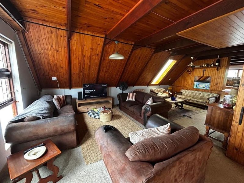 Spacious living area featuring a vaulted timber ceiling with exposed beams, wood-paneled walls, and a skylight, creating a warm and rustic atmosphere.
