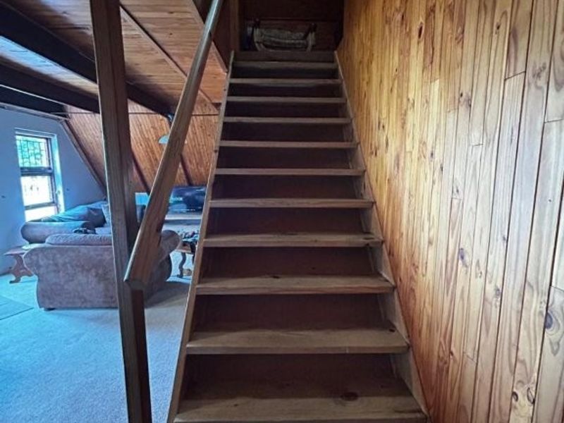 A wooden staircase featuring timber wall paneling and exposed ceiling beams, leading to an upper level within the home.