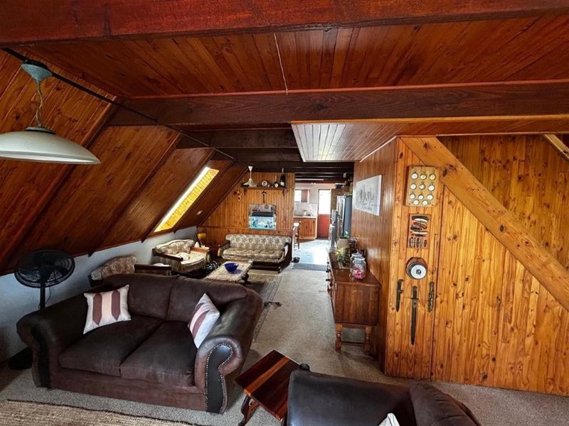 Open-plan living area featuring extensive timber wall and ceiling paneling, a skylight, and integrated storage, leading through to the kitchen area.