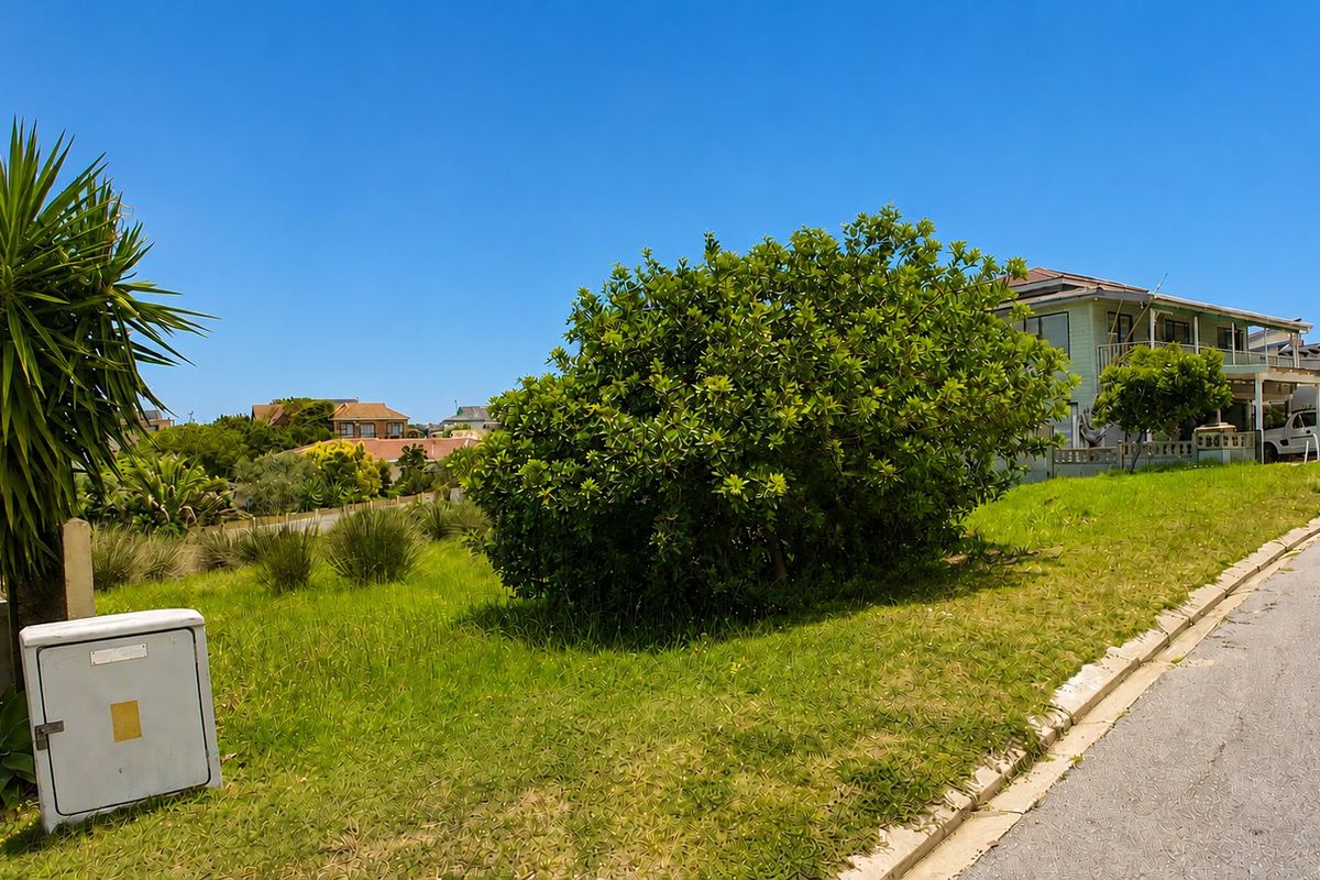 A view of a vacant residential plot featuring a grassy landscape, an electrical utility box, and street-side infrastructure in a suburban neighborhood.