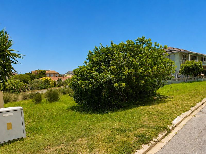 A view of a vacant residential plot featuring a grassy landscape, an electrical utility box, and street-side infrastructure in a suburban neighborhood.
