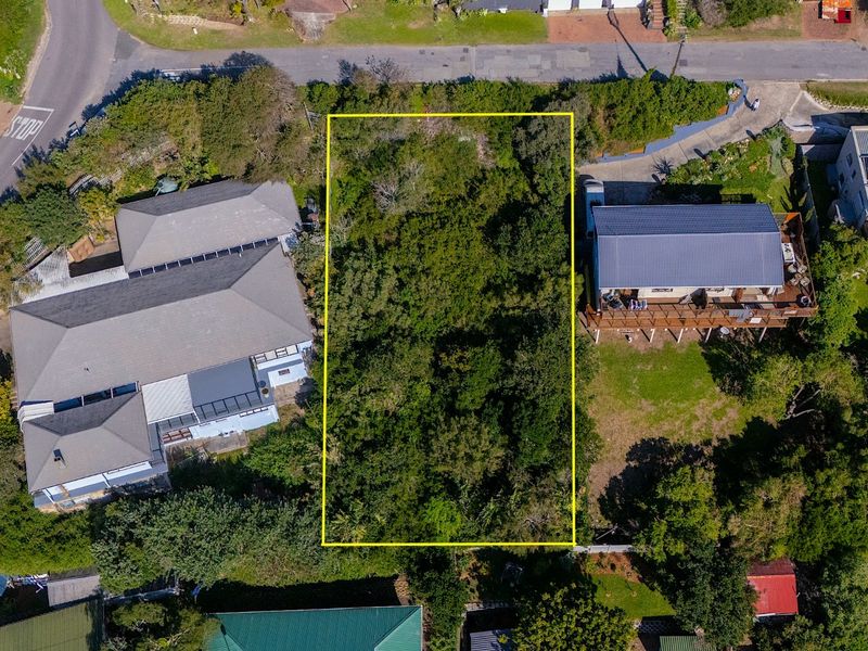 An aerial view of a vacant residential plot highlighted in yellow, surrounded by established residential properties and dense vegetation.