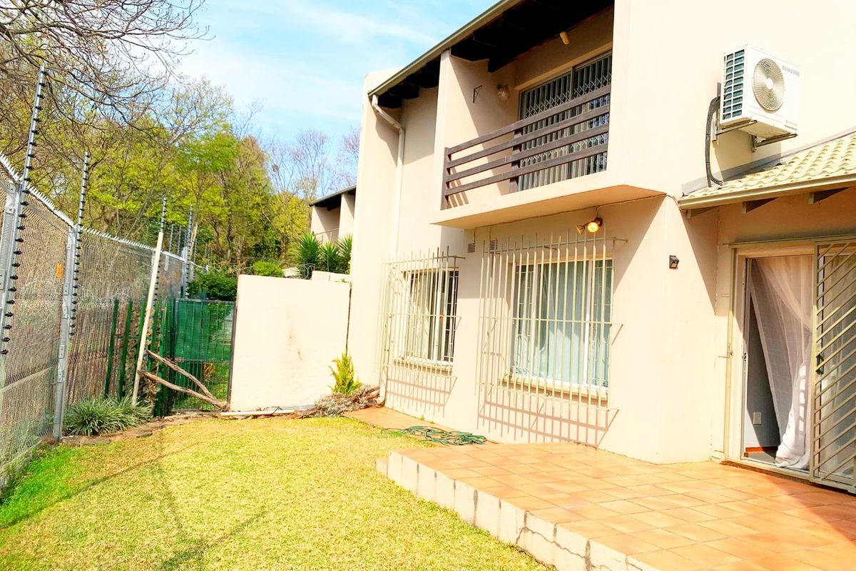 Rear view of the apartment featuring a tiled patio, upper-level balcony, security bars on windows, and an enclosed garden area with electric fencing.