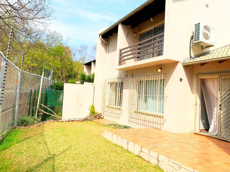 Rear view of the apartment featuring a tiled patio, upper-level balcony, security bars on windows, and an enclosed garden area with electric fencing.
