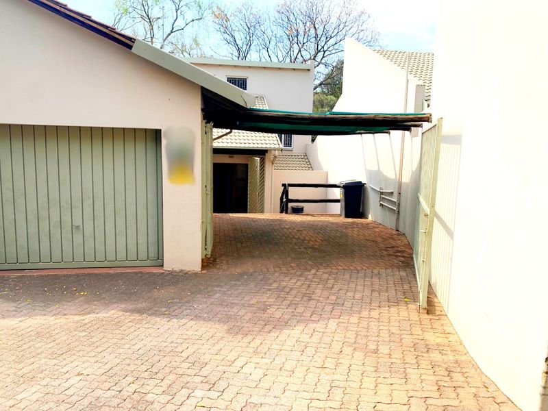 Exterior view of the property featuring a paved driveway, a garage, and a shade cloth awning providing covered parking space.