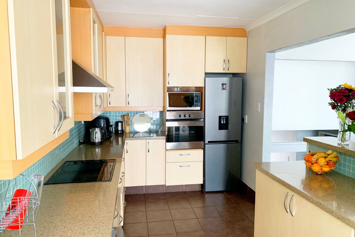 A functional kitchen featuring light wood cabinetry, stone countertops, a tiled backsplash, and integrated appliances including an oven, microwave, and hob.