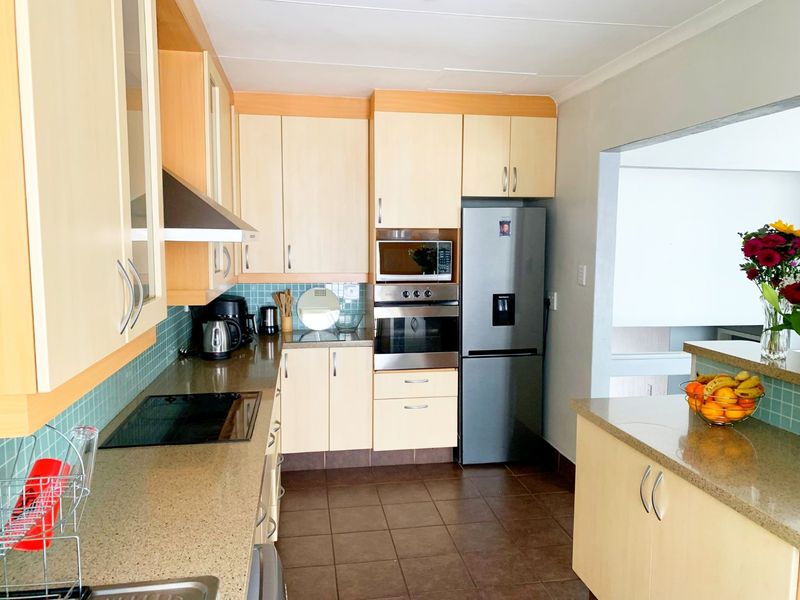 A functional kitchen featuring light wood cabinetry, stone countertops, a tiled backsplash, and integrated appliances including an oven, microwave, and hob.