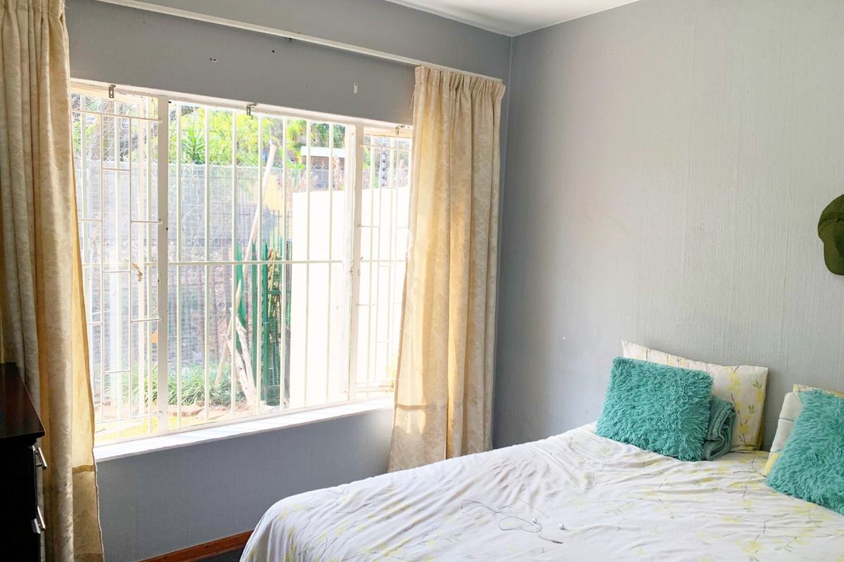 A bedroom featuring a large window with security bars, neutral wall paint, and classic skirting boards, offering a functional space with natural light.