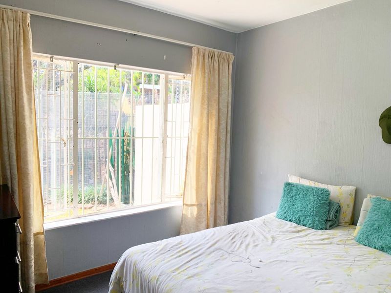 A bedroom featuring a large window with security bars, neutral wall paint, and classic skirting boards, offering a functional space with natural light.
