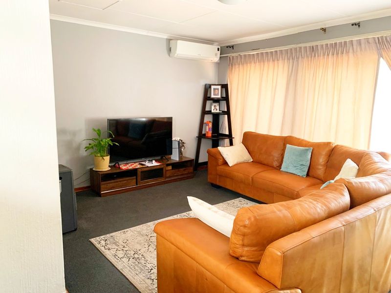 A comfortable living room featuring carpet flooring, neutral wall tones, and a wall-mounted split-system air conditioner for climate control.