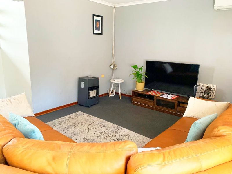 A comfortable living room featuring neutral wall finishes, carpeted flooring, and a wall-mounted air conditioning unit.