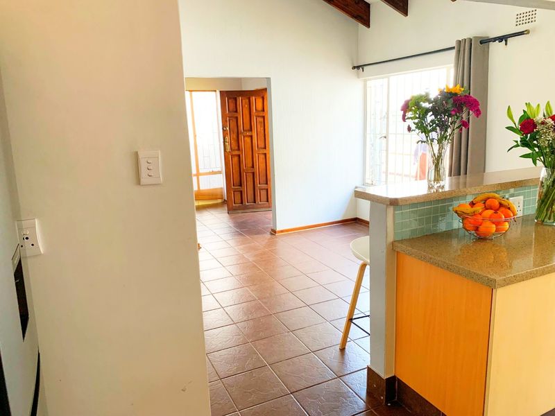 Open plan living area featuring tiled flooring, exposed timber ceiling beams, and a kitchen breakfast bar with stone countertops and a tiled backsplash.