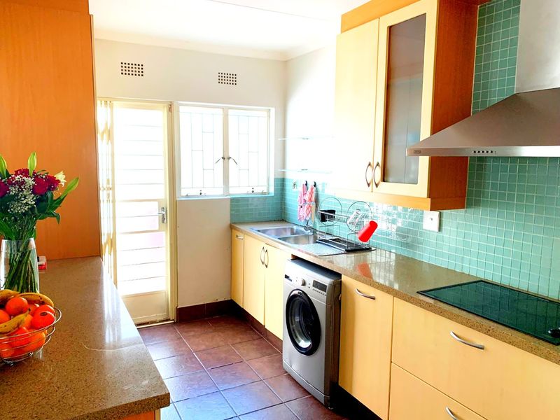 A functional kitchen featuring laminate cabinetry, stone countertops, a tiled backsplash, and integrated cooking appliances with direct access to an exterior door.