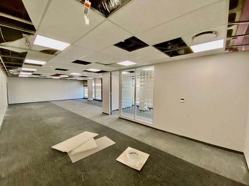 Open plan commercial office space featuring a suspended ceiling with missing tiles, glass partitioning, and carpeted flooring, currently in need of maintenance and repair.