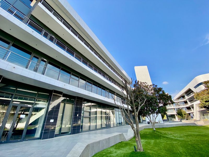 Modern commercial office building featuring a glass facade, multiple levels of balconies, and a well-maintained landscaped lawn area.