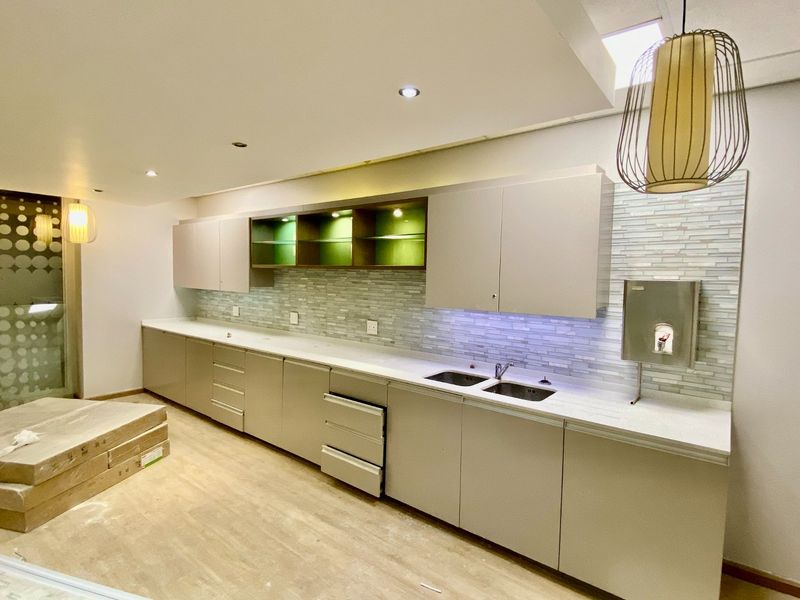Modern commercial kitchen area featuring sleek built-in cabinetry, stone countertops, a double sink, and stylish mosaic tile backsplash with integrated lighting.