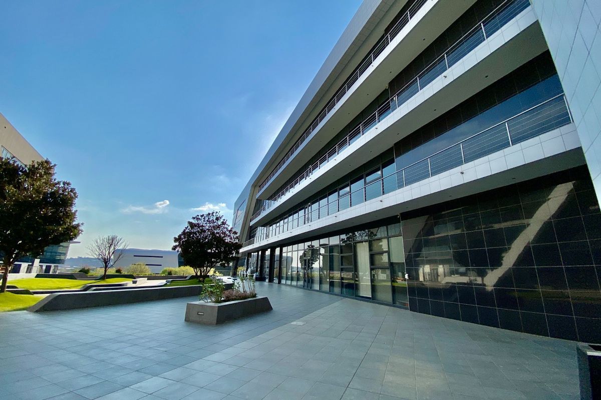 A modern multi-story commercial office building featuring a spacious tiled patio, glass curtain walls, and sleek metal balcony railings.