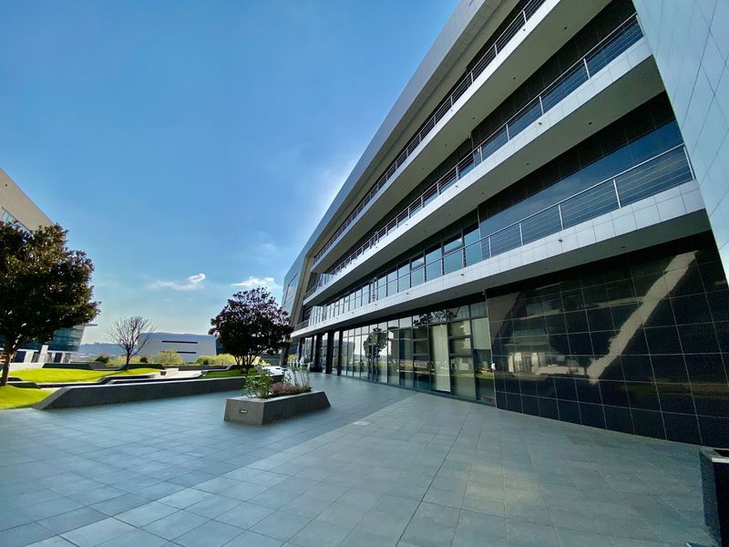 A modern multi-story commercial office building featuring a spacious tiled patio, glass curtain walls, and sleek metal balcony railings.