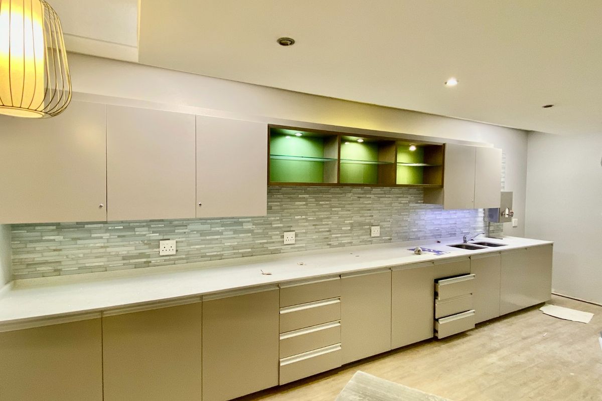 Modern kitchen featuring sleek built-in cabinetry, stone countertops, a decorative mosaic tile backsplash, and integrated display shelving with ambient lighting.