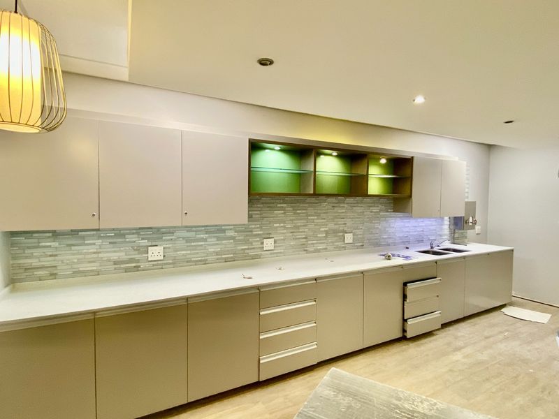 Modern kitchen featuring sleek built-in cabinetry, stone countertops, a decorative mosaic tile backsplash, and integrated display shelving with ambient lighting.
