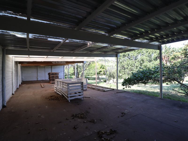 A spacious covered outdoor patio area featuring a corrugated metal roof, steel support structure, and concrete flooring, overlooking the surrounding farm landscape.