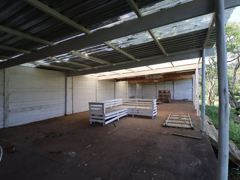 A spacious covered outdoor patio area featuring a corrugated metal roof with translucent panels, timber support posts, and concrete flooring.