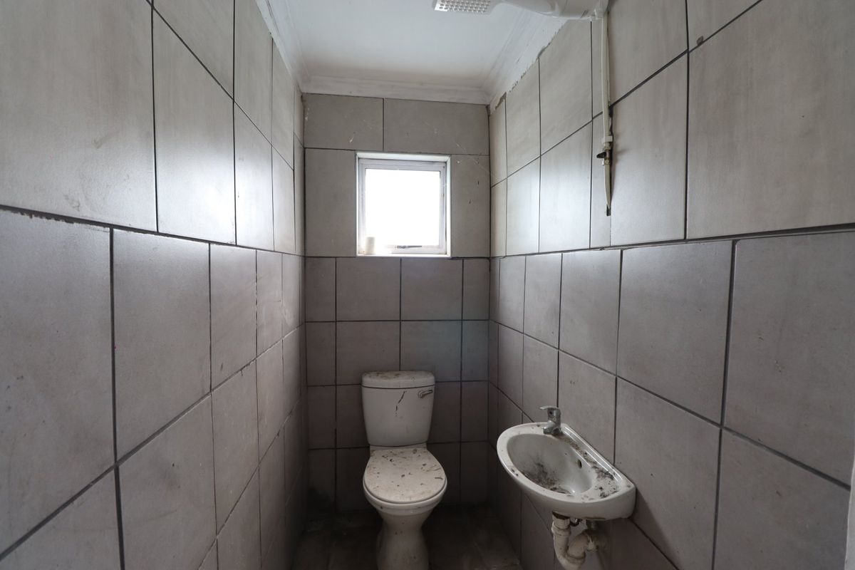 A small, tiled bathroom featuring a toilet and wall-mounted basin, currently in need of significant cleaning and cosmetic refurbishment.