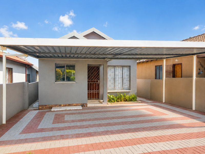 Front elevation of the house featuring a paved driveway, a covered carport, and secure entrance with security gate and window bars.