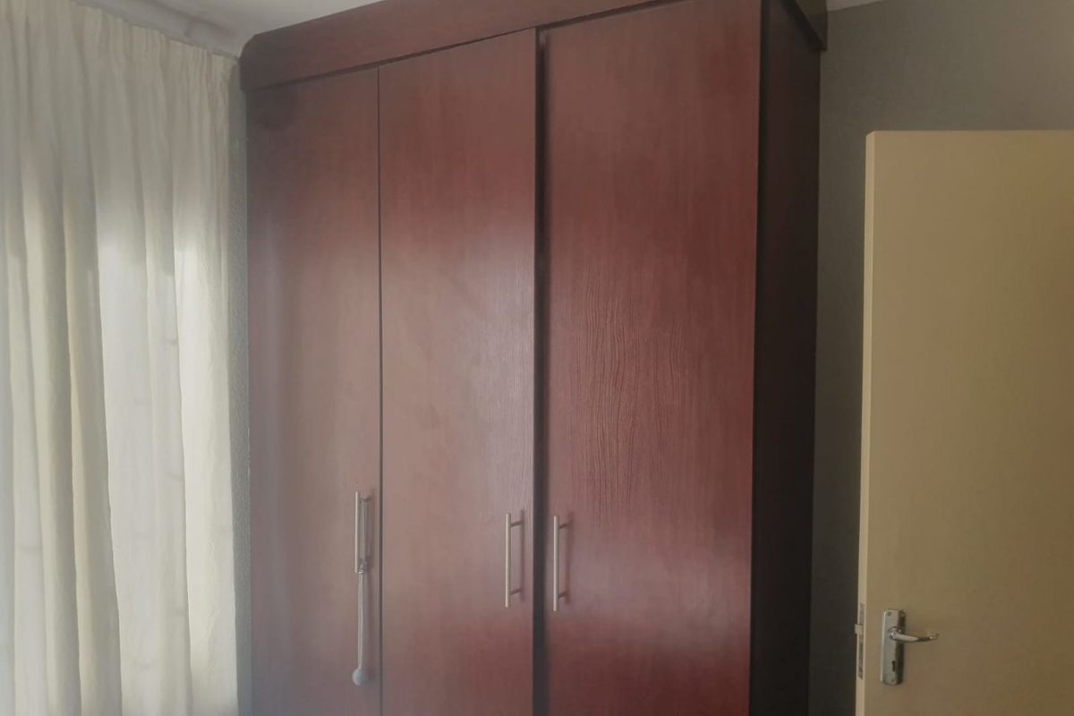 A bedroom featuring a large, dark wood built-in wardrobe with modern metal handles and a curtained window.