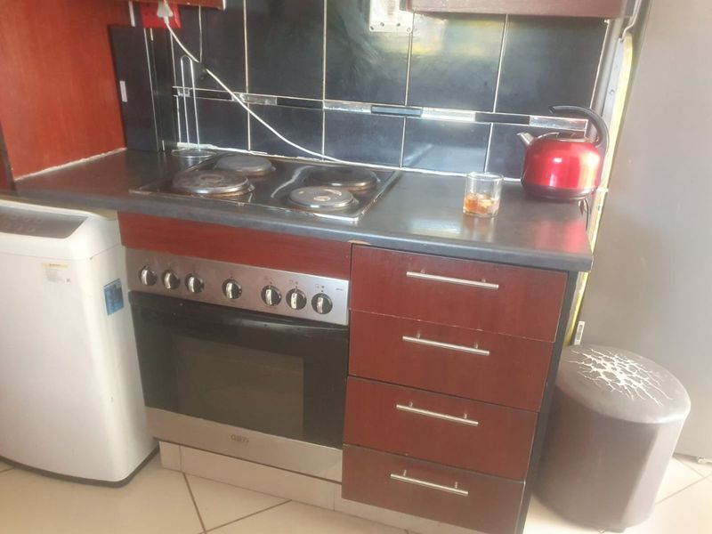 A compact kitchen area featuring a built-in oven, electric hob, dark laminate cabinetry, and a tiled backsplash.