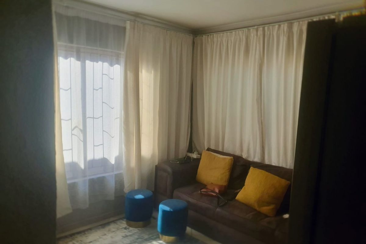 A living room area featuring natural light through windows with security bars and curtain tracks.