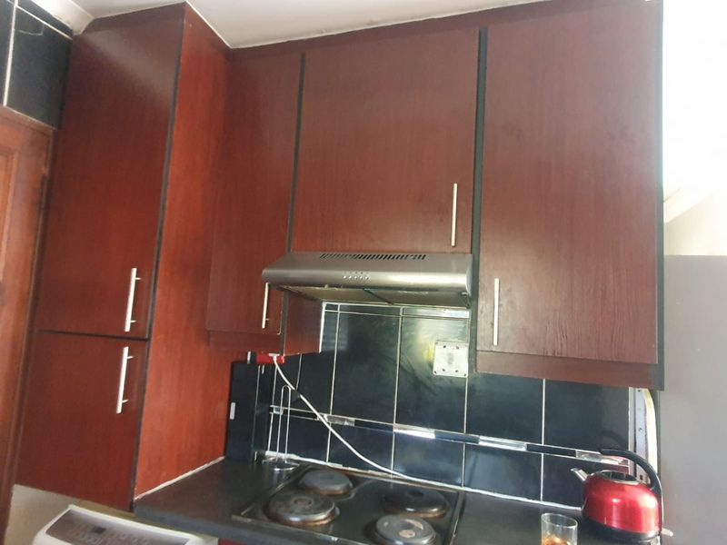 A kitchen area featuring dark wood-finish cabinetry, a built-in extractor fan, an electric hob, and a black tiled backsplash.