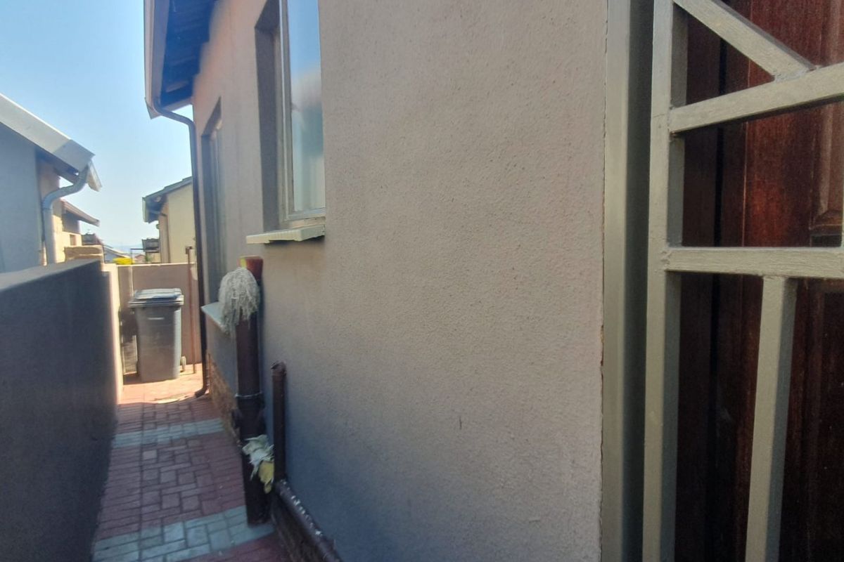 A side exterior walkway featuring paved flooring, a security gate, and a plastered wall with a window.
